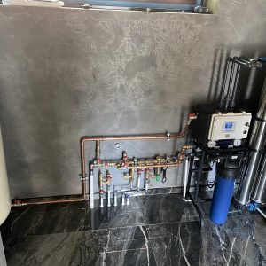 Copper and stainless steel water filtration system with multi-stage filters and pressure gauges in a modern indoor setting.